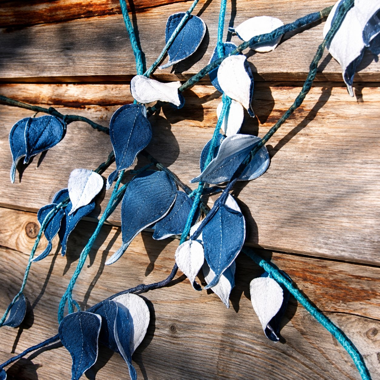 Des branches ornées de feuilles bleues et blanches sont fixées contre un mur en planches de bois.