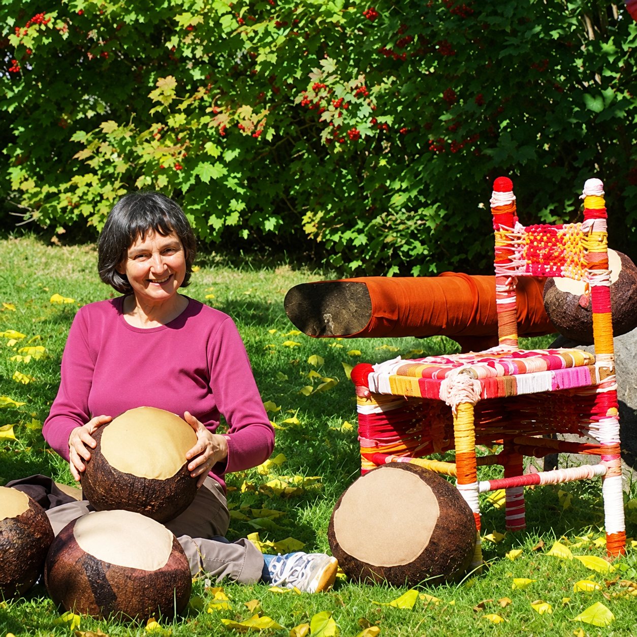 Michèle Dallon assise dans l’herbe près d’une chaise tissée